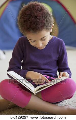 Stock Photo - Mixed race girl reading on bedroom floor. Fotosearch