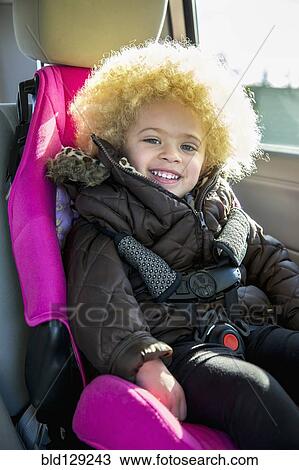 Stock Image - Mixed race girl smiling in back seat of car. Fotosearch