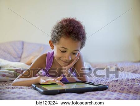 Picture - Mixed race girl using digital tablet in bed. Fotosearch