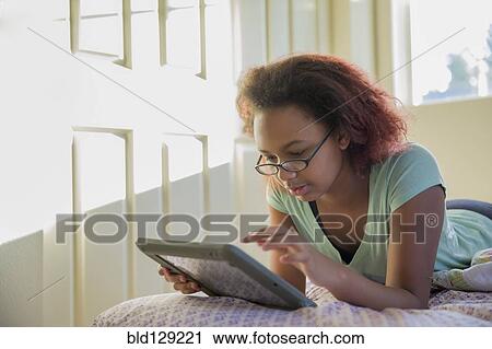 Stock Image - Mixed race girl using digital tablet in bed. Fotosearch