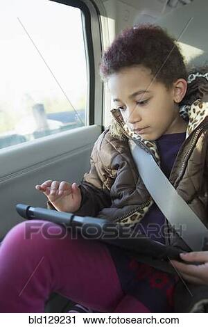 Stock Image - Mixed race girl using digital tablet in back seat of car. Fotosearch