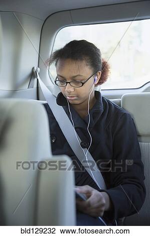 Stock Image - Mixed race girl using digital tablet in back seat of car. Fotosearch