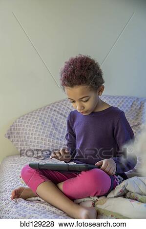 Stock Photo - Mixed race girl using digital tablet in bed. Fotosearch