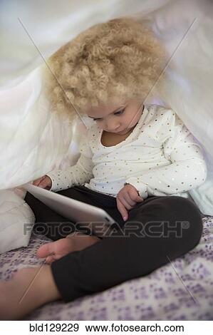 Stock Photo - Mixed race girl using digital tablet under covers. Fotosearch