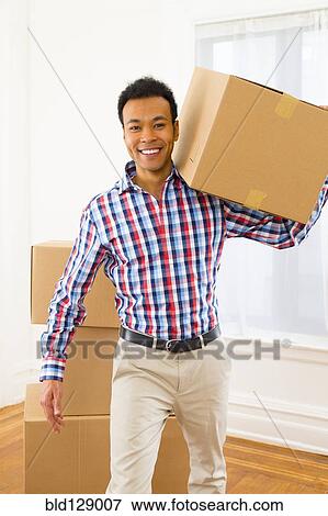Stock Photo - Mixed race man carrying cardboard box in new home. Fotosearch