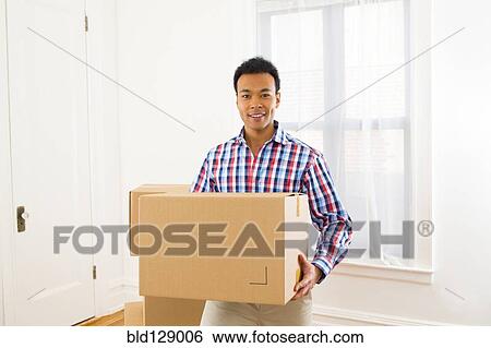 Stock Photograph - Mixed race man carrying cardboard box in new home. Fotosearch