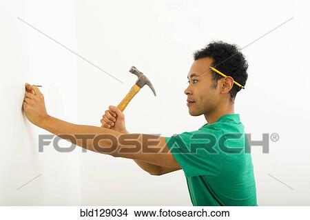 Picture - Mixed race man hammering nail into wall. Fotosearch