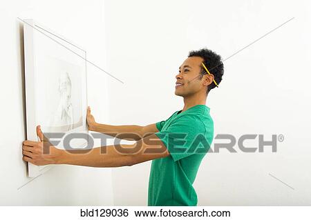 Mixed race man hanging picture on wall View Large Photo Image Stock Photograph - Mixed race man hanging picture on wall. Fotosearch