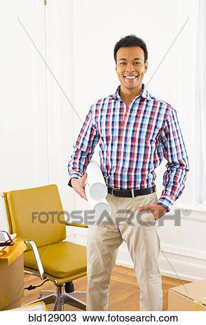Stock Image - Mixed race man holding blueprints. Fotosearch