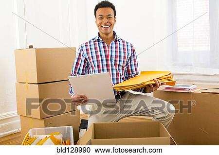 Stock Image - Mixed race man packing cardboard boxes. Fotosearch
