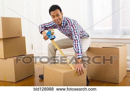 Stock Photo - Mixed race man packing cardboard boxes. Fotosearch