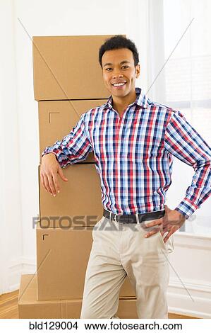 Mixed race man standing by cardboard boxes in new home View Large Photo Image Picture - Mixed race man standing by cardboard boxes in new home. Fotosearch