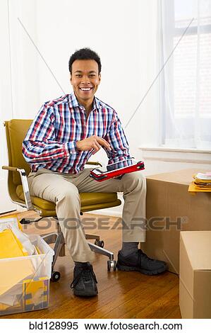 Stock Photography - Mixed race man using digital tablet in new home. Fotosearch