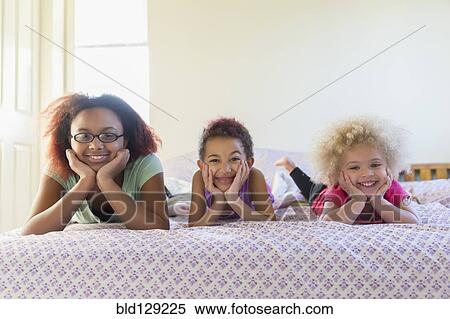 Stock Photography - Mixed race sisters laying in bed. Fotosearch