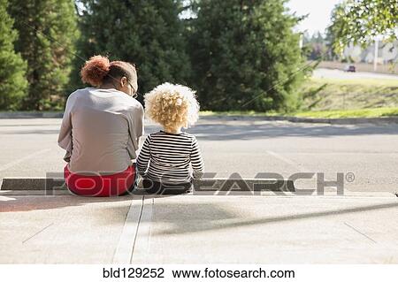 Stock Image - Mixed race sisters sitting outdoors. Fotosearch