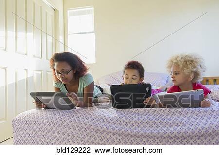 Mixed race sisters using digital tablets in bed View Large Photo Image Stock Image - Mixed race sisters using digital tablets in bed. Fotosearch