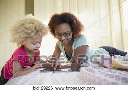Mixed race sisters using digital tablet in bed View Large Photo Image Stock Photograph - Mixed race sisters using digital tablet in bed. Fotosearch