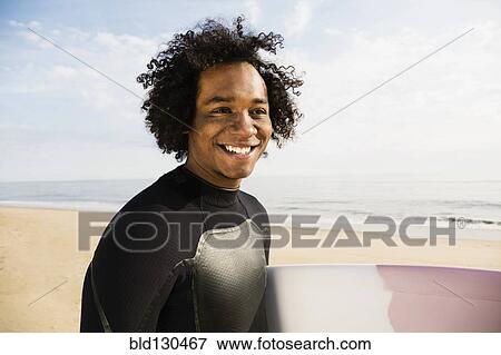 Mixed race surfer carrying board on beach View Large Photo Image Stock Photo - Mixed race surfer carrying board on beach. Fotosearch
