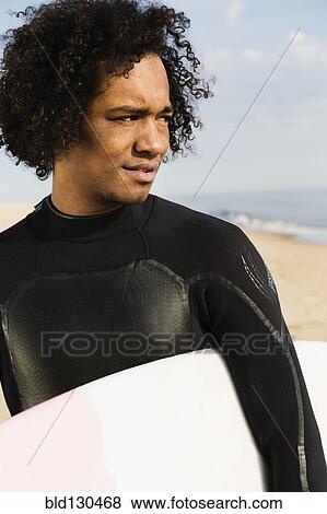 Mixed race surfer carrying board on beach View Large Photo Image Stock Photo - Mixed race surfer carrying board on beach. Fotosearch