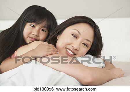 Stock Photograph - Mother and daughter laying on bed. Fotosearch