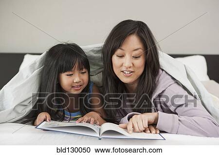 Stock Image - Mother and daughter reading in bed. Fotosearch