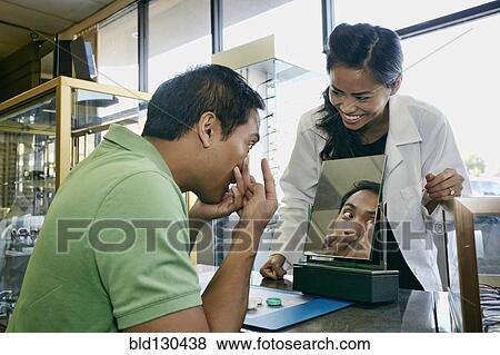 Stock Photo - Optometrist helping patient with contacts in office. Fotosearch