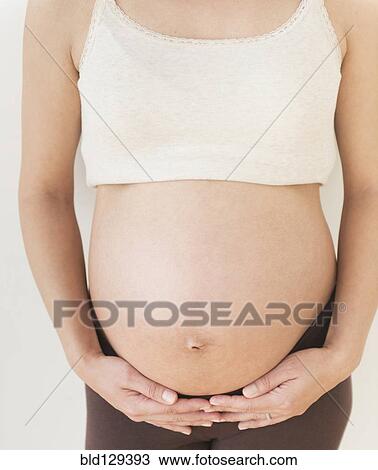 Stock Image - Pregnant Hispanic woman holding her belly. Fotosearch