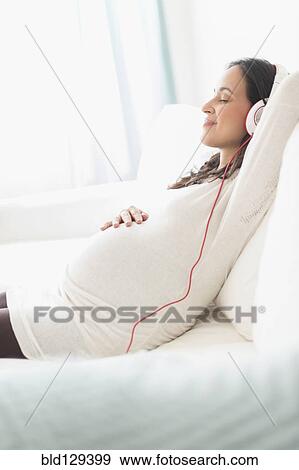 Stock Photo - Pregnant Hispanic woman listening to headphones. Fotosearch