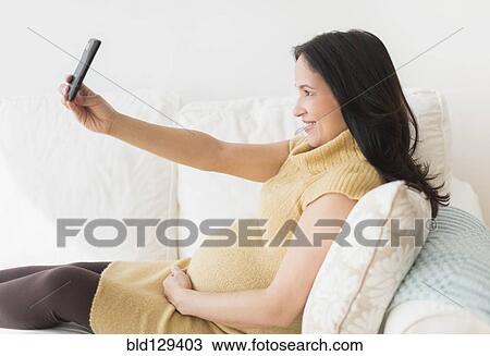 Stock Image - Pregnant Hispanic woman taking picture with cell phone. Fotosearch