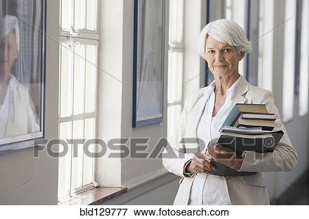 Stock Photo - Senior Caucasian businesswoman carrying books in office. Fotosearch