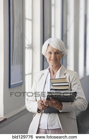 Stock Photograph - Senior Caucasian businesswoman carrying books in office. Fotosearch