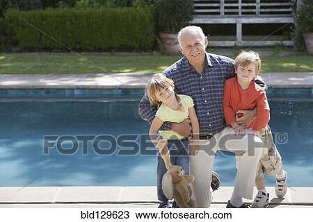 Stock Image - Senior Caucasian man hugging grandchildren by pool. Fotosearch
