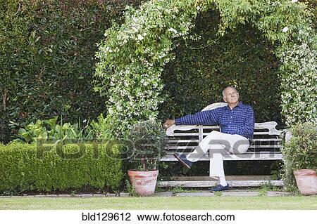 Stock Image - Senior Caucasian man sitting on garden bench. Fotosearch