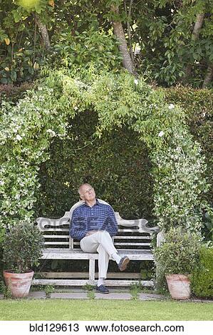 Stock Image - Senior Caucasian man sitting on garden bench. Fotosearch