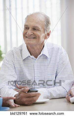 Stock Image - Senior Caucasian man using cell phone in cafe. Fotosearch
