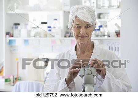 Stock Image - Senior Caucasian scientist using microscope in lab. Fotosearch