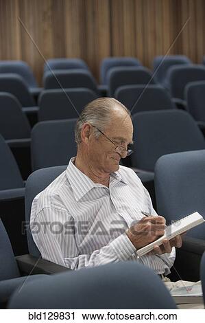 Stock Image - Senior Caucasian student taking notes in classroom. Fotosearch