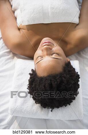 Stock Image - Serene Black woman laying on massage table. Fotosearch