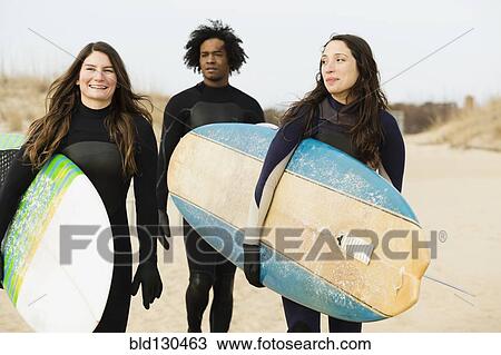 Stock Image - Surfers carrying boards on beach. Fotosearch