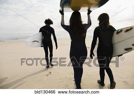 Stock Photograph - Surfers carrying boards on beach. Fotosearch