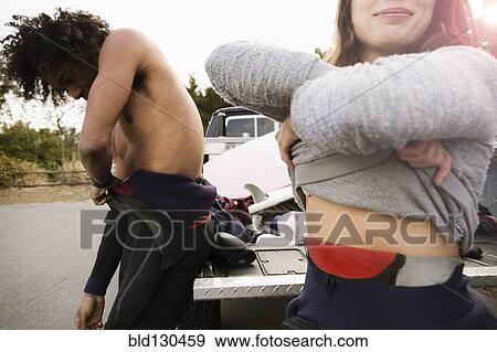 Stock Photo - Surfers pulling on wet suits by truck. Fotosearch