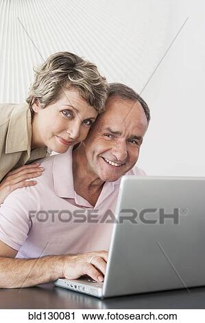 Stock Image - Woman hugging husband at laptop. Fotosearch