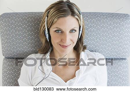 Woman listening to headphones in armchair View Large Photo Image Stock Image - Woman listening to headphones in armchair. Fotosearch