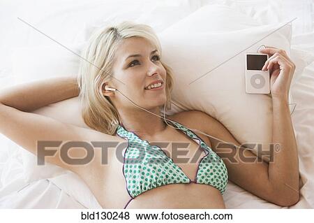 Stock Photo - Woman listening to mp3 player on bed. Fotosearch