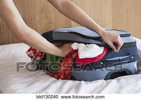 Stock Image - Woman packing suitcase on bed. Fotosearch