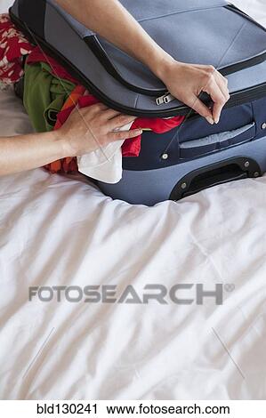 Stock Image - Woman packing suitcase on bed. Fotosearch