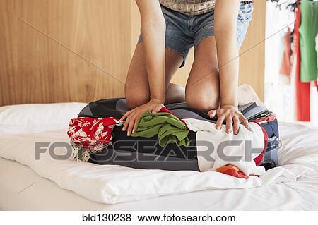 Stock Photo - Woman packing suitcase on bed. Fotosearch
