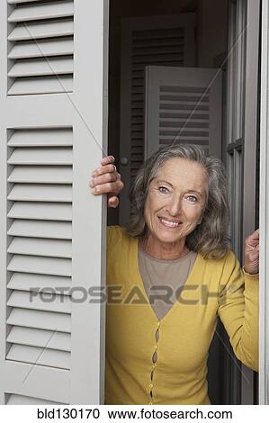Stock Image - Woman peering out window shutters. Fotosearch
