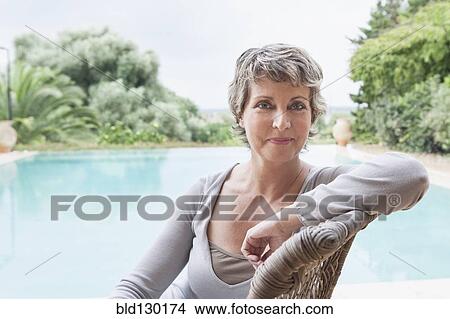 Picture - Woman smiling in armchair by swimming pool. Fotosearch