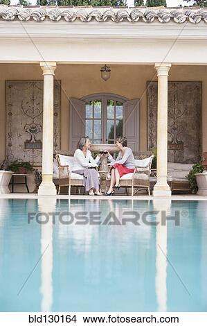 Women toasting each other by swimming pool View Large Photo Image Picture - Women toasting each other by swimming pool. Fotosearch